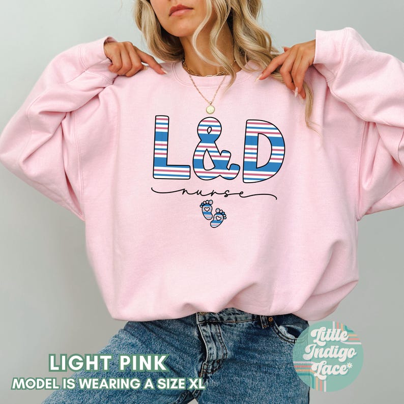 May include: Light pink sweatshirt with the text "L&D nurse" in blue and red stripes with a pair of baby footprints below the text.