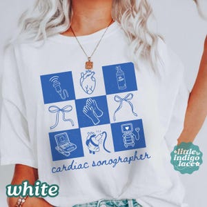 May include: A white t-shirt featuring a blue grid graphic with medical icons including a heart, ultrasound probe, gel bottle, gloves, and sonography machine. The text "cardiac sonographer" is printed in blue script below the grid design.