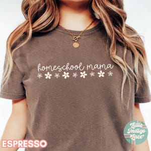 May include: A brown t-shirt with the text "homeschool mama" in white lettering. A row of white daisies are below the text.