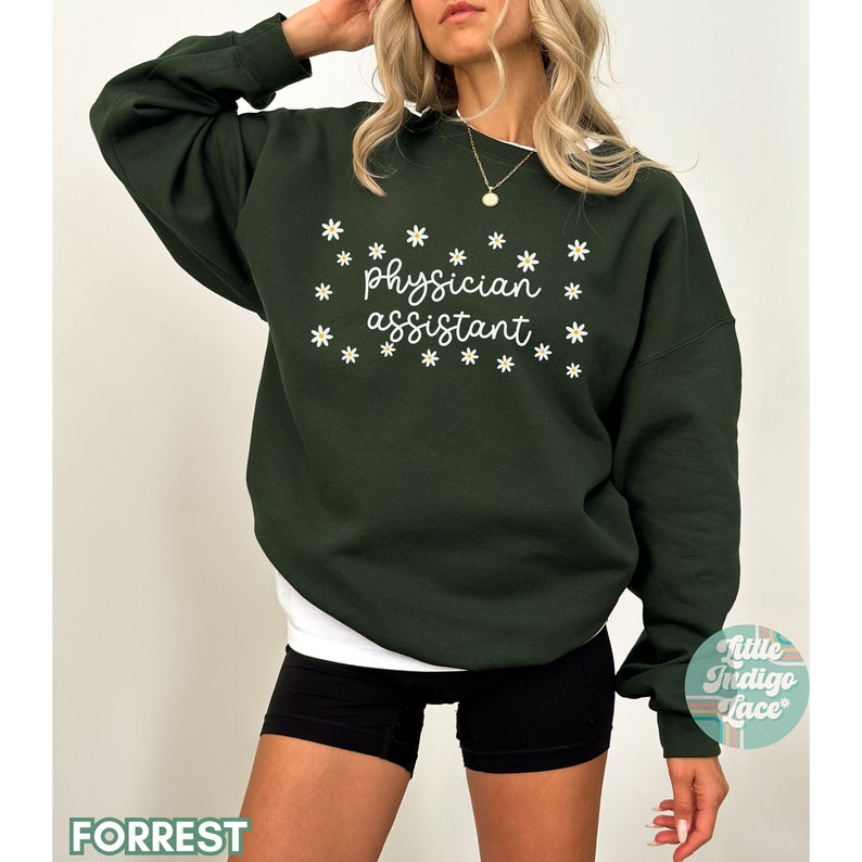 May include: A dark green sweatshirt with the text "physician assistant" in white lettering surrounded by white daisy flowers.