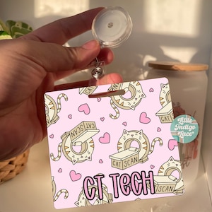 May include: Pink retractable badge holder featuring a cartoon cat design. The badge holder has a pink background with white hearts and cats in a CT scan machine. The text "CAT SCAN" and "CT TECH" are printed on the badge holder.