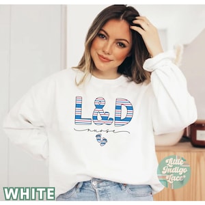 May include: White sweatshirt with blue and red striped letters that spell "L&D nurse" with a small footprint graphic below.