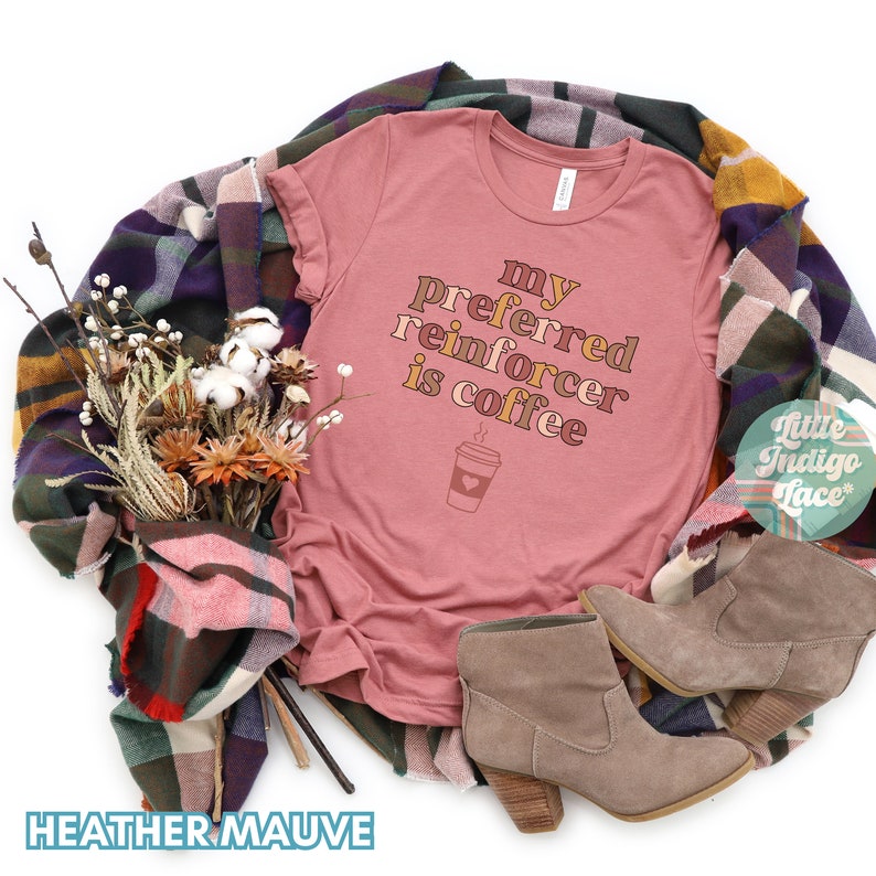 May include: Heather mauve t-shirt with the text "my preferred reinforcer is coffee" in a retro font. A cartoon coffee cup with a heart is below the text.