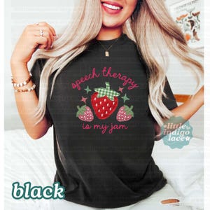K&ouml;nnte beinhalten: Schwarzes T-Shirt mit dem Text "speech therapy is my jam" in rosa Schrift. Das Design zeigt eine gro&szlig;e rote Erdbeere mit einem gr&uuml;n karierten Oberteil und zwei kleineren Erdbeeren. Das Wort "black" steht unten.
