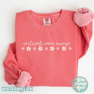May include: A pink sweatshirt with the text "critical care nurse" in white lettering and a row of white daisies below the text. The sweatshirt is folded in half and the sleeves are rolled up.