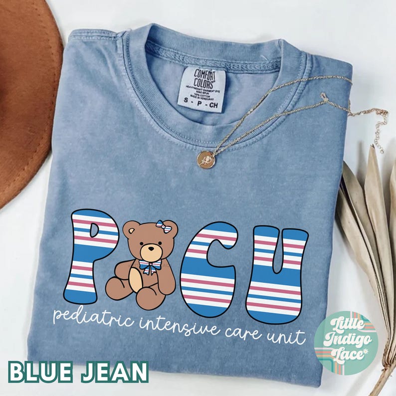 May include: Blue jean t-shirt with a graphic of a teddy bear and the text "PCU pediatric intensive care unit".
