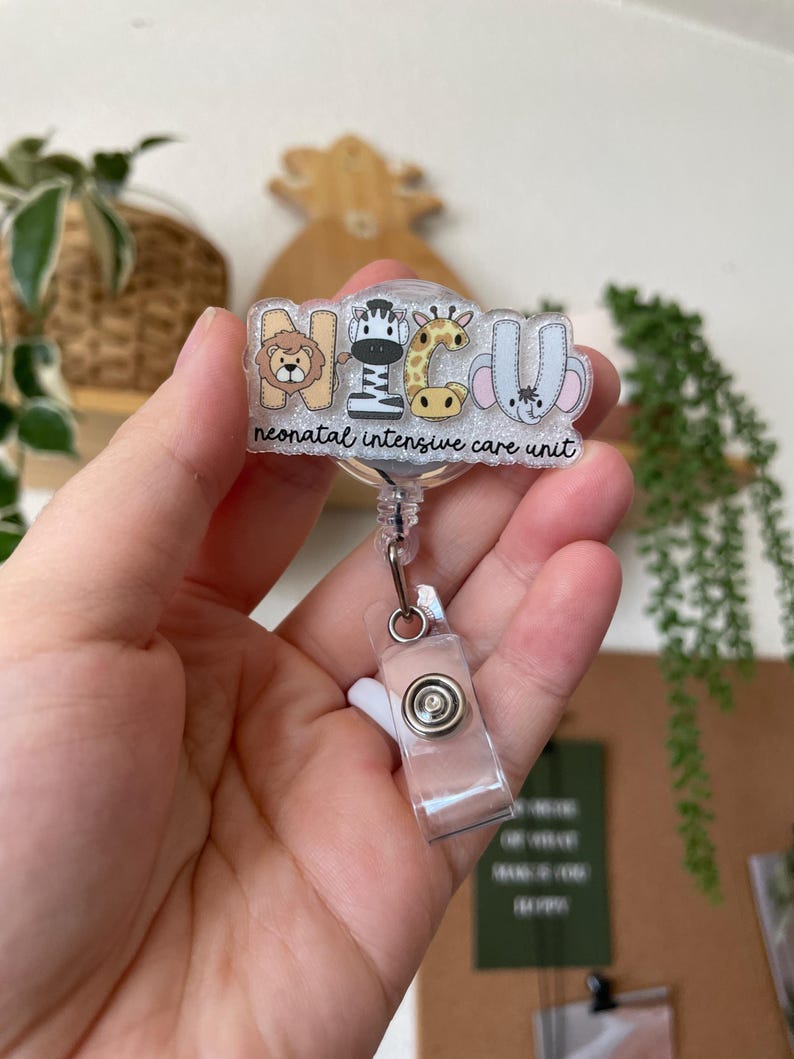 May include: A clear badge reel with the letters "NICU" and animal illustrations. The text "neonatal intensive care unit" is below the letters. The reel has a clear plastic clip and a silver metal button.