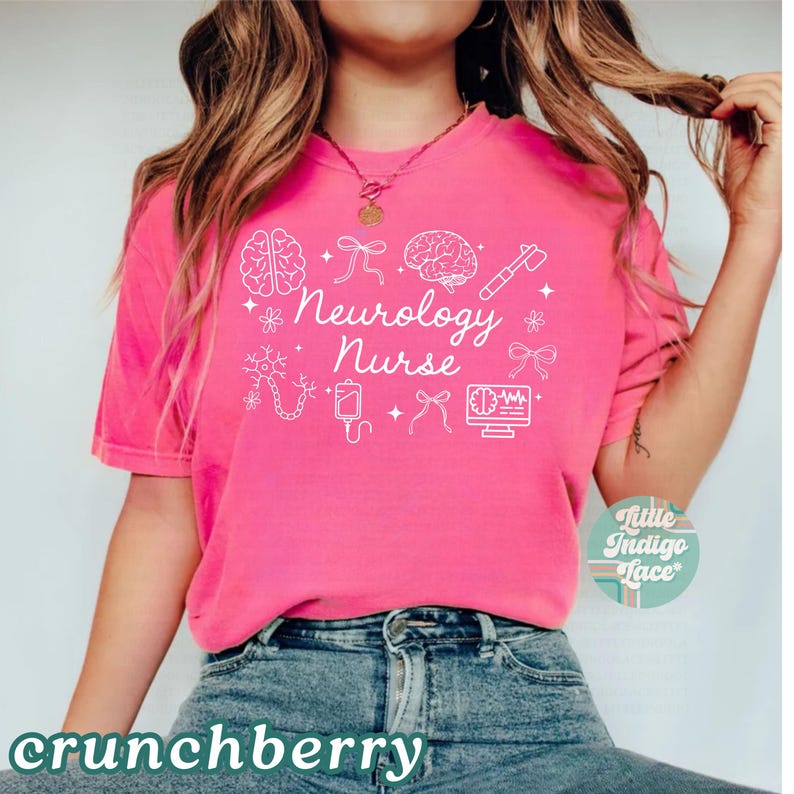 May include: A bright pink t-shirt with the words "Neurology Nurse" in white script, surrounded by white medical-themed illustrations. The shirt has a crew neck and short sleeves. The word "crunchberry" is at the bottom.