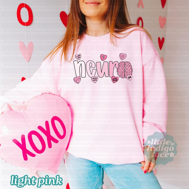 May include: Light pink sweatshirt with the word "neur" in a checkered pattern and a brain graphic. The sweatshirt has several heart-shaped candies with phrases like "I love you" and "XOXO". A pink heart-shaped balloon with "XOXO" is also visible.