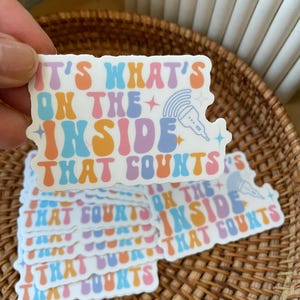 May include: A stack of colorful stickers with the text "It's what's on the inside that counts". The stickers have a retro, groovy font and are decorated with stars and a microphone.