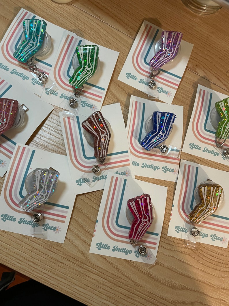 Pu&ograve; includere: Assortimento di porta badge retrattili pieni di glitter colorati con un design a gamba di scheletro bianco. Ogni porta badge &egrave; attaccato a una carta con il testo "Little Indigo Lace".
