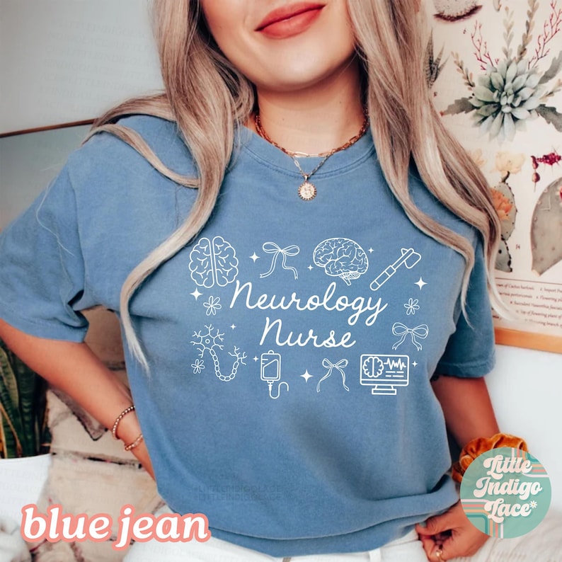 May include: A blue jean colored t-shirt with the words "Neurology Nurse" in white script, along with white illustrations of a brain, medical tools, and other medical symbols. The shirt has short sleeves.