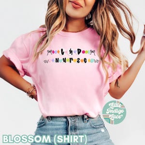 K&ouml;nnte beinhalten: Rosa T-Shirt mit dem Text "I  <3  DOGS  NURSE" in schwarzen Buchstaben mit bunten Verzierungen.