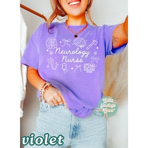 May include: Violet-colored t-shirt with the words "Neurology Nurse" and various medical-themed graphics in white. The shirt is a comfortable fit and is paired with blue jeans. The word "violet" is printed at the bottom.