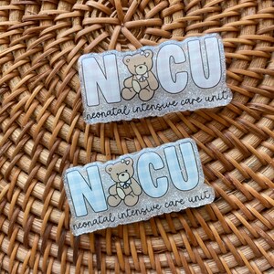 May include: Two rectangular badges with the letters "NCU" in white, with a teddy bear illustration. The background of the letters is a light blue and white gingham pattern. The text "neonatal intensive care unit" is below the letters.