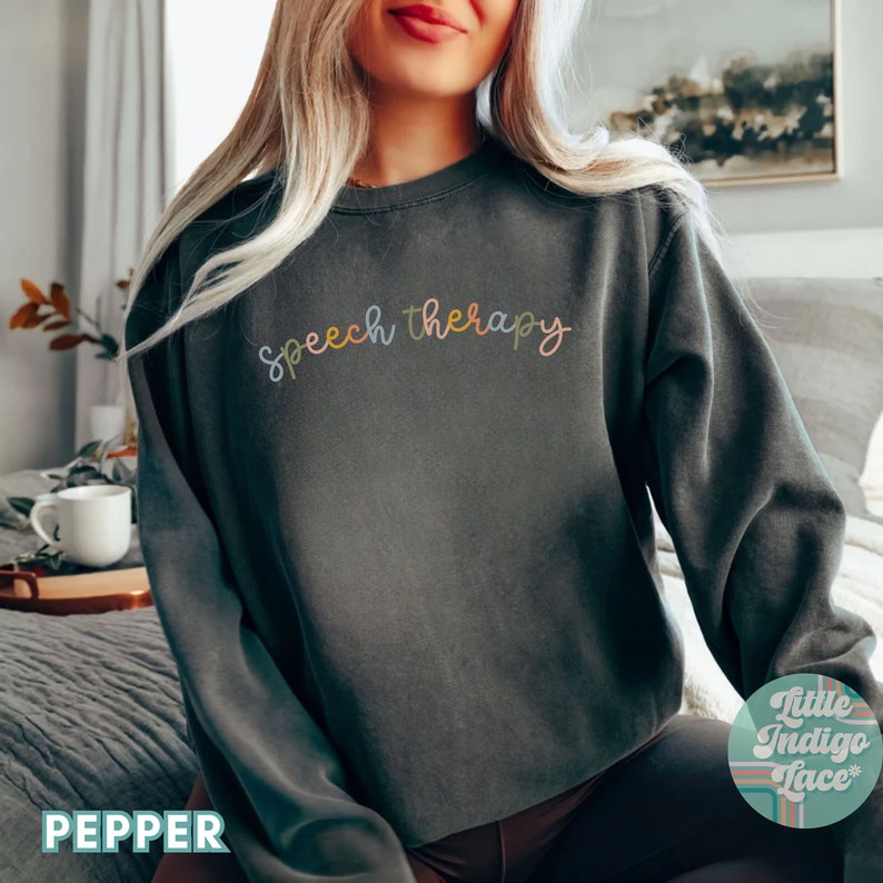 May include: A dark gray sweatshirt with the text "speech therapy" written in colorful script across the front.