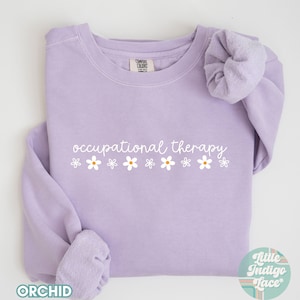 May include: A lavender sweatshirt with the text "occupational therapy" and a row of white daisies printed on the front.