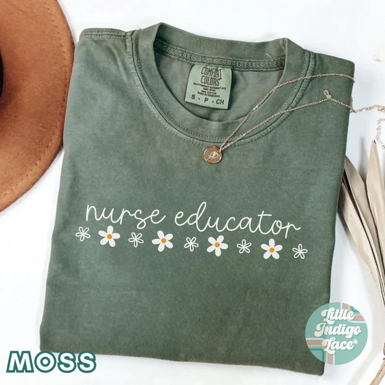 以下が含まれることがあります： モスグリーンのTシャツに、白い文字で「nurse educator」と書いてあり、その下に白いデイジーの花が並んでいます。このTシャツは柔らかく快適な素材で作られており、ゆったりとしたフィット感です。
