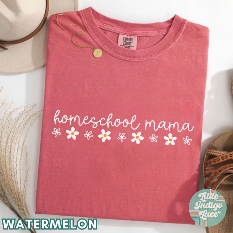 May include: Watermelon-colored t-shirt with the text "homeschool mama" in white lettering and a row of white daisies with yellow centers.