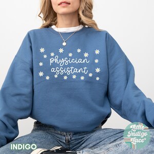 May include: A blue sweatshirt with the text "physician assistant" in white lettering and a pattern of white daisies.