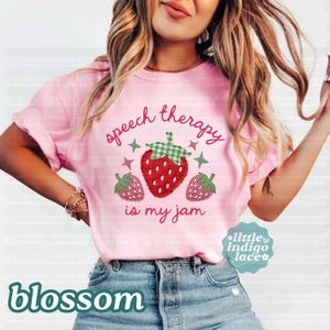 K&ouml;nnte beinhalten: Hellrosa T-Shirt mit dem Text "speech therapy is my jam" und einer Erdbeer-Grafik. Die Erdbeere hat einen gr&uuml;n karierten Deckel und ist von gr&uuml;nen Sternen und zwei kleineren Erdbeeren umgeben.