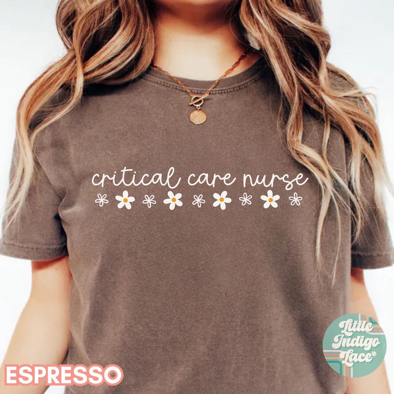 Puede incluir: Una camiseta marr&oacute;n con el texto "critical care nurse" en letras blancas y una fila de margaritas blancas debajo del texto.