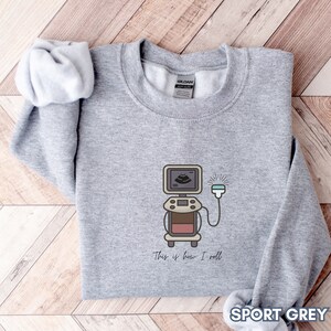 May include: Sport grey sweatshirt with a cartoon ultrasound machine graphic. The graphic includes the text "This is how I roll". The sweatshirt is made of a soft material.