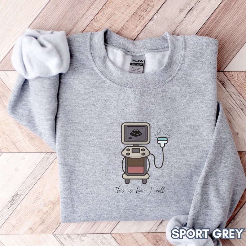 May include: Sport grey sweatshirt with a cartoon ultrasound machine graphic. The graphic includes the text "This is how I roll". The sweatshirt is made of a soft material.