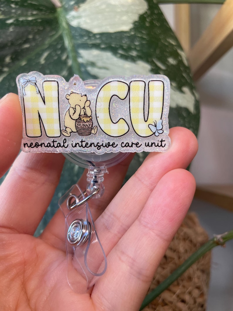 May include: A badge reel with the letters "NCU" in yellow gingham print, featuring a cartoon bear and the words "neonatal intensive care unit". The reel has a clear plastic clip and a retractable cord.