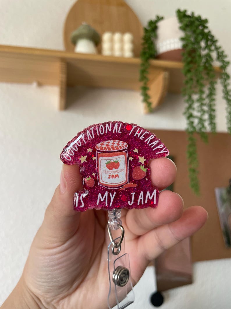 Puede incluir: Portagafete de purpurina rosa con un dise&ntilde;o de tarro de mermelada de fresa y el texto "Occupational Therapy is my jam".