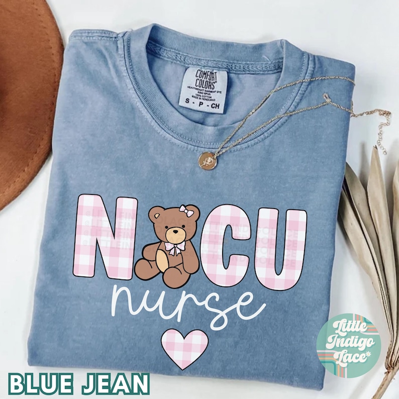 Puede incluir: Una camiseta de mezclilla azul con las palabras "NICU nurse" en estampado de cuadros rosa y blanco. Un coraz&oacute;n de cuadros rosa est&aacute; debajo del texto. Un oso de peluche de dibujos animados con un lazo rosa est&aacute; en el medio del texto.