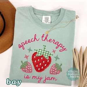 K&ouml;nnte beinhalten: Hellgr&uuml;nes T-Shirt mit dem pinkfarbenen Schriftzug "speech therapy is my jam", einer gro&szlig;en roten Erdbeere und zwei kleineren Erdbeeren. Die Erdbeerbl&auml;tter sind gr&uuml;n und wei&szlig; kariert. Das Shirt hat ein Comfort Colors-Etikett.