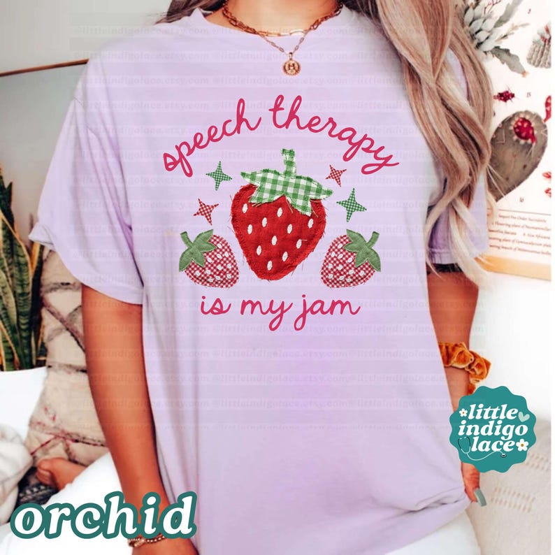 K&ouml;nnte beinhalten: Lilafarbenes T-Shirt mit dem Schriftzug "speech therapy is my jam" in rosa Schrift. Das Shirt zeigt eine gro&szlig;e Erdbeer-Grafik mit einem gr&uuml;n karierten Oberteil und zwei kleineren Erdbeer-Grafiken.