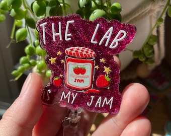 May include: A glittery dark pink badge reel featuring a central illustration of a strawberry jam jar with a red and white checkered lid. The text reads THE LAB IS MY JAM in white lettering, surrounded by small yellow stars and strawberry icons.