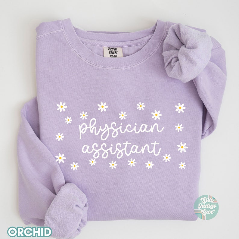 May include: A lavender sweatshirt with the text "physician assistant" in white lettering surrounded by white daisy flowers.