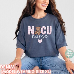 Puede incluir: Una camiseta de gran tama&ntilde;o de color azul denim con el texto "NICU nurse" en letras a cuadros rosas y blancas. Tambi&eacute;n hay un coraz&oacute;n rosa y un oso de peluche de dibujos animados en la camiseta.