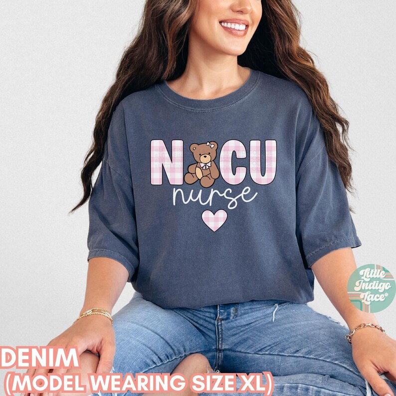 Puede incluir: Una camiseta de gran tama&ntilde;o de color azul denim con el texto "NICU nurse" en letras a cuadros rosas y blancas. Tambi&eacute;n hay un coraz&oacute;n rosa y un oso de peluche de dibujos animados en la camiseta.