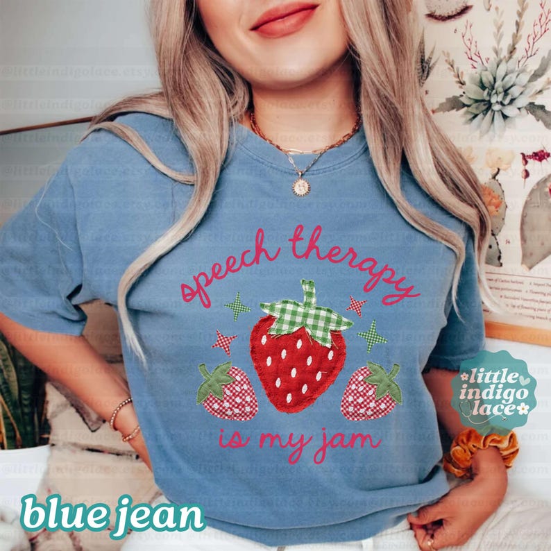 K&ouml;nnte beinhalten: Blaues Jeans-T-Shirt mit dem Text "speech therapy is my jam" und einer Erdbeer-Grafik. Die Erdbeere hat einen roten K&ouml;rper und eine gr&uuml;n-wei&szlig; karierte Spitze. Zwei kleinere Erdbeeren sind ebenfalls abgebildet.