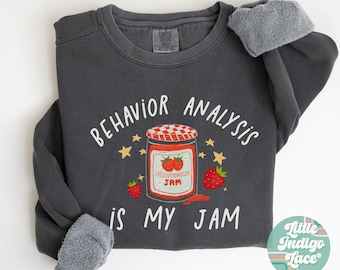 May include: A dark gray sweatshirt with the text "Behavior Analysis is My Jam" in white. The text is surrounded by stars and a jar of strawberry jam with the text "Strawberry Jam" on the label.
