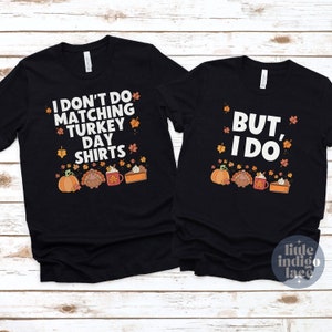 Może przedstawiać: Dwie czarne koszulki z białym napisem i jesiennymi grafikami. Na lewej koszulce widnieje napis I DON'T DO MATCHING TURKEY DAY SHIRTS, a na prawej BUT, I DO. Obie zawierają ilustracje dyni, indyka, kubka oraz kawałka ciasta.