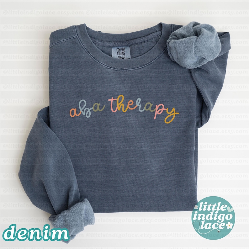 K&ouml;nnte beinhalten: Ein denimblaues Comfort Colors Sweatshirt mit dem Schriftzug "aba therapy" in farbenfroher Schrift. Das Sweatshirt hat eine lockere Passform und gerollte B&uuml;ndchen. Das Wort "denim" ist unten aufgedruckt.