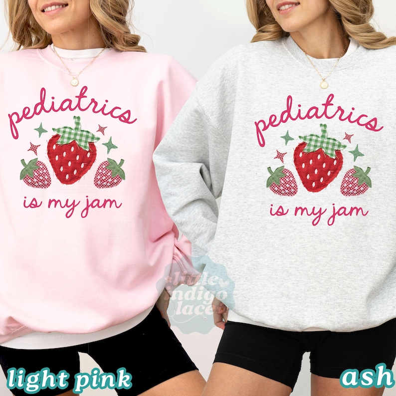May include: A light pink sweatshirt and a light gray sweatshirt, each featuring the red text "pediatrics is my jam" and a graphic of a large red strawberry with a green checkered top, flanked by two smaller strawberries and four-pointed star accents.