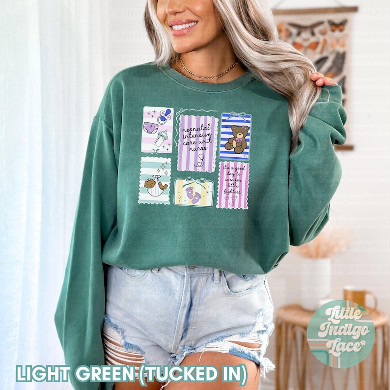 Puede incluir: Sudadera verde claro con un dise&ntilde;o gr&aacute;fico que presenta ilustraciones relacionadas con beb&eacute;s y texto. El texto incluye "neonatal intensive care unit nurse" y "It's a good day to care for little fighters".