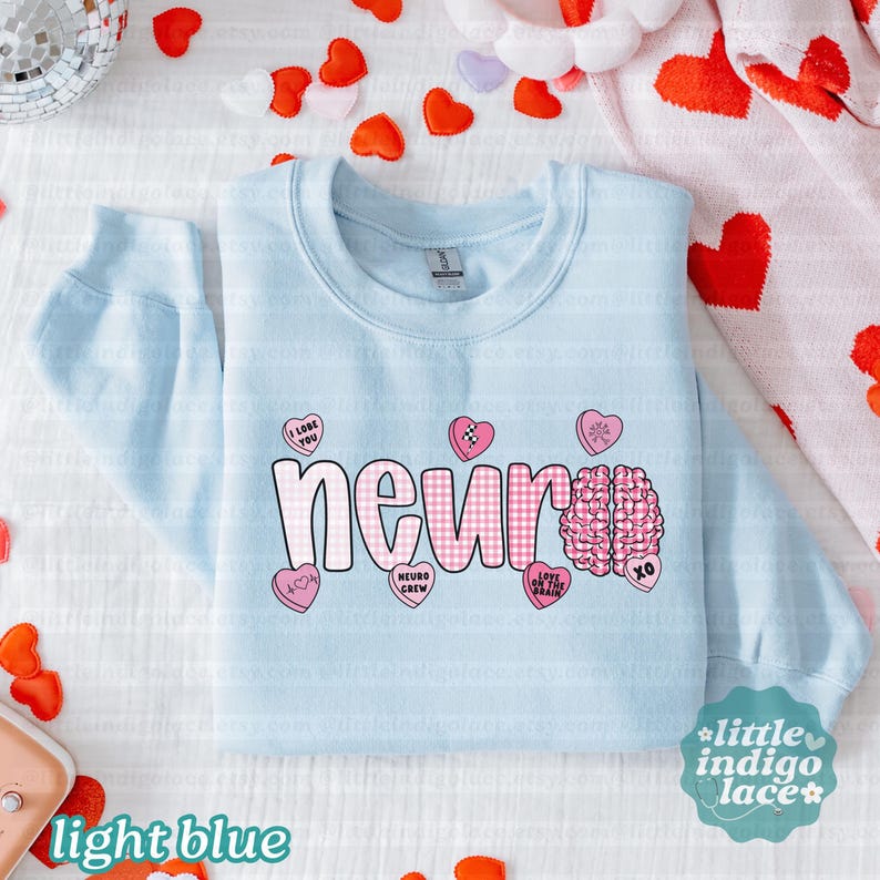 May include: Light blue sweatshirt with the word "neur" in white letters and a pink gingham pattern. Pink heart-shaped candies with phrases like "I love you" and a brain graphic are also featured. The words "light blue" are at the bottom.