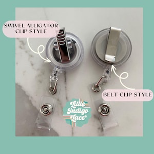 May include: Two clear badge reels with different clip styles. One has a swivel alligator clip, and the other has a belt clip. The reels have a clear plastic body with a retractable cord and a clear plastic snap. The text "Little Indigo Lace" is also visible.