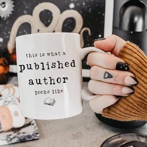 May include: White ceramic mug with black text that reads "this is what a published author looks like" and a small black and white illustration of an open book.