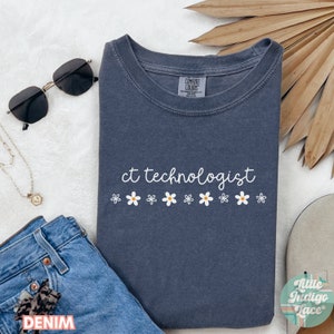 May include: A dark blue t-shirt with the text "ct technologist" in white script and a row of white daisies with yellow centers below the text.