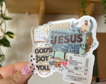 May include: A clear sticker with the words "GOD'S GOT YOU" and "JESUS" in a collage design. The sticker includes images of doves, a heart, a cross, and text that reads "JESUS PAID IT ALL".