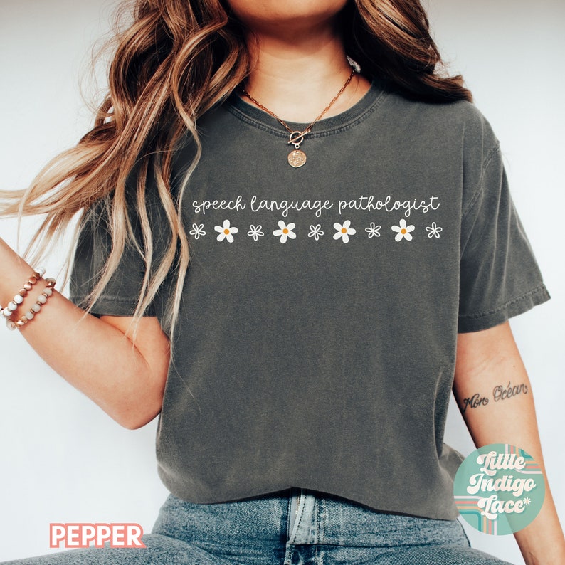 May include: A dark gray t-shirt with the text "speech language pathologist" and a row of white daisies.