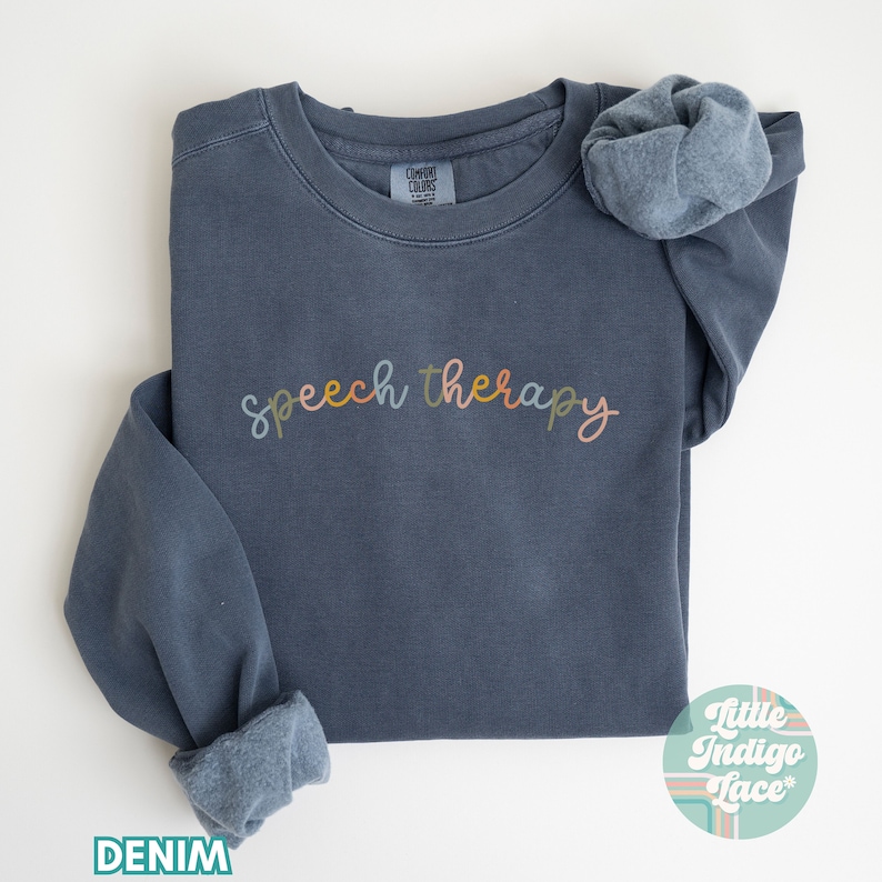 May include: A dark blue sweatshirt with the text "speech therapy" in colorful lettering. The sweatshirt is made of a soft, comfortable fabric and has a relaxed fit.